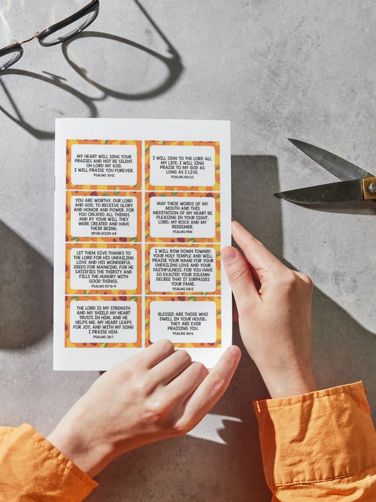 hands holding printed scripture cards with scissors.